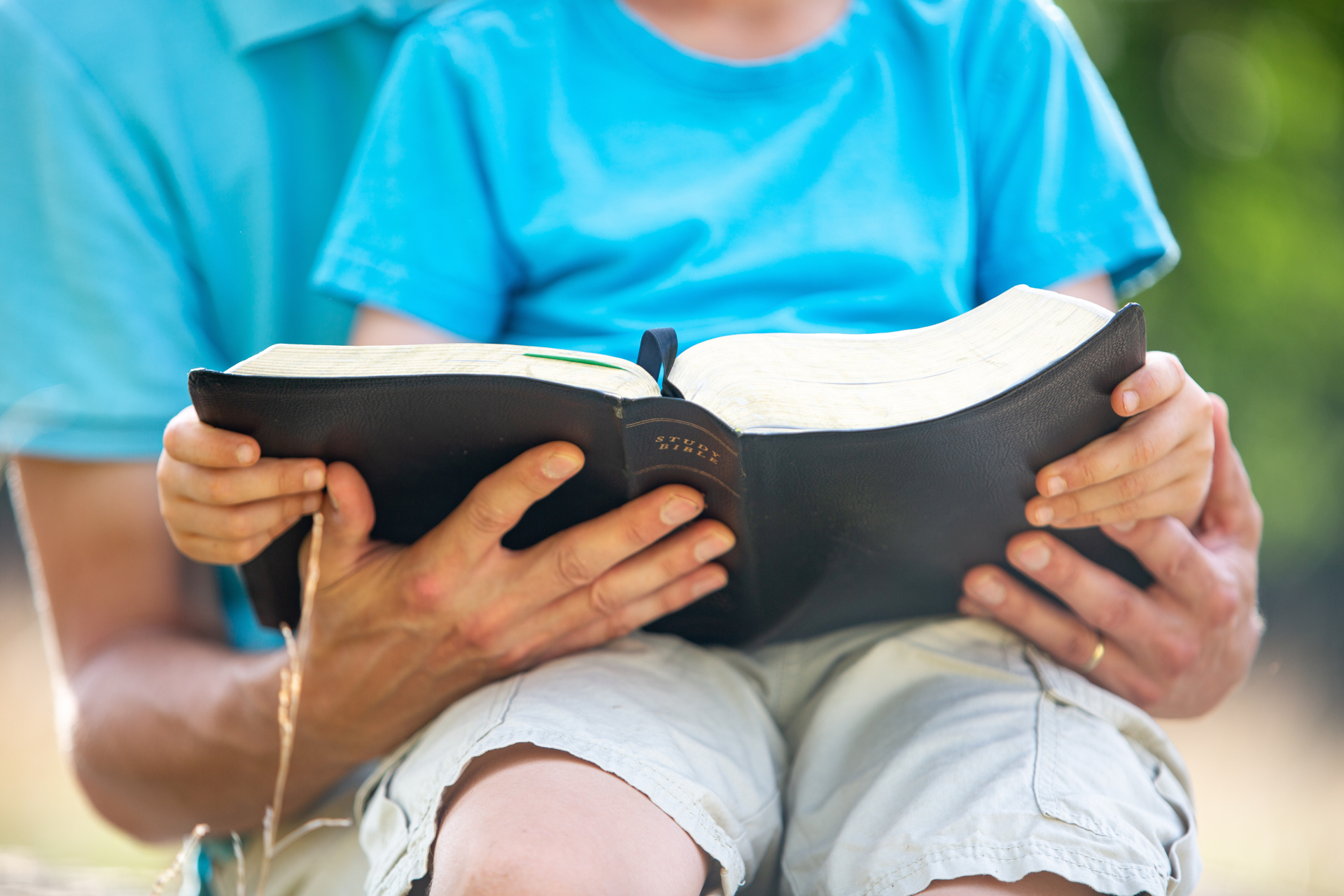 Adult and child hands holding open study bible together.